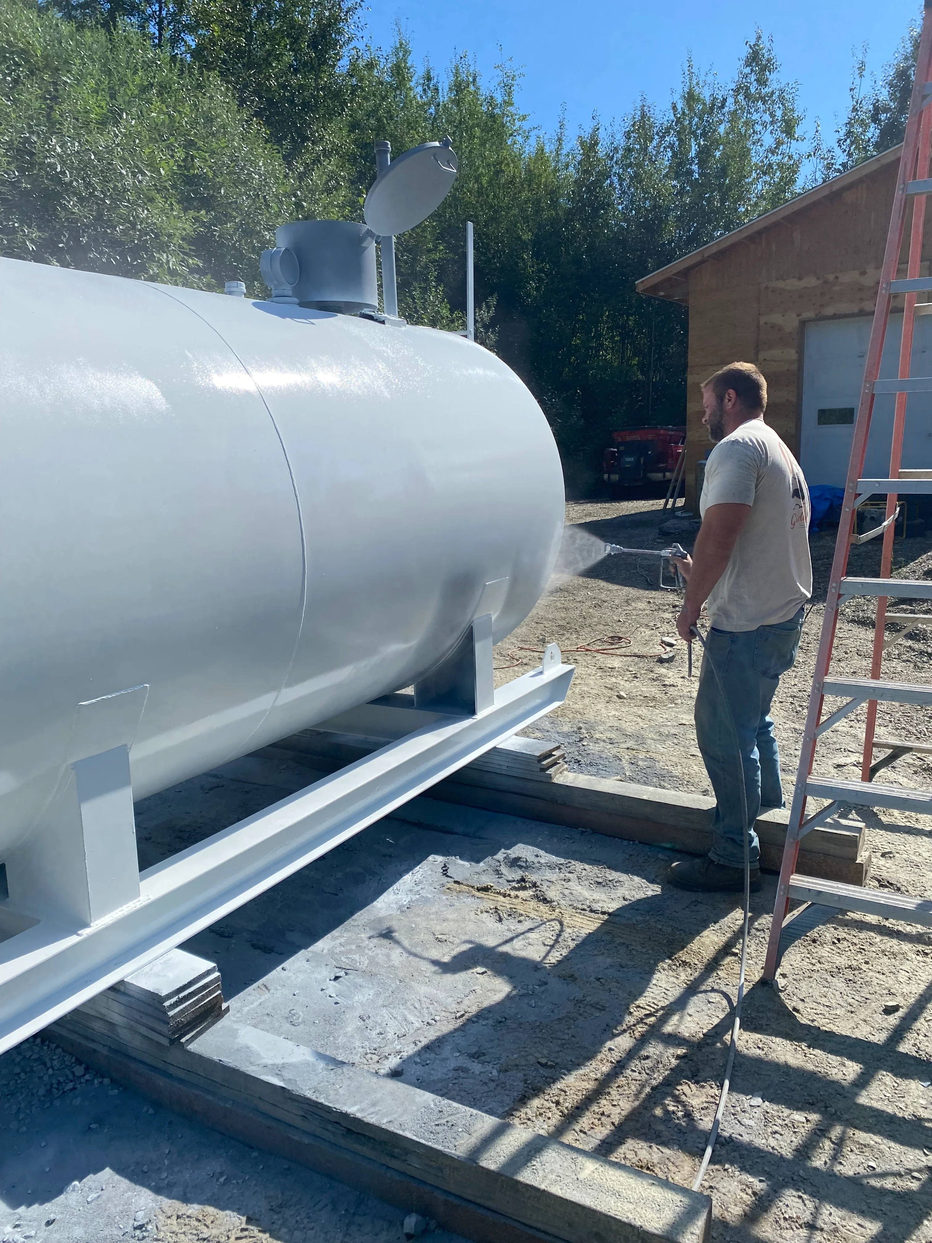 White propane tank with regulators on concrete pad, steel frame base and access ladder