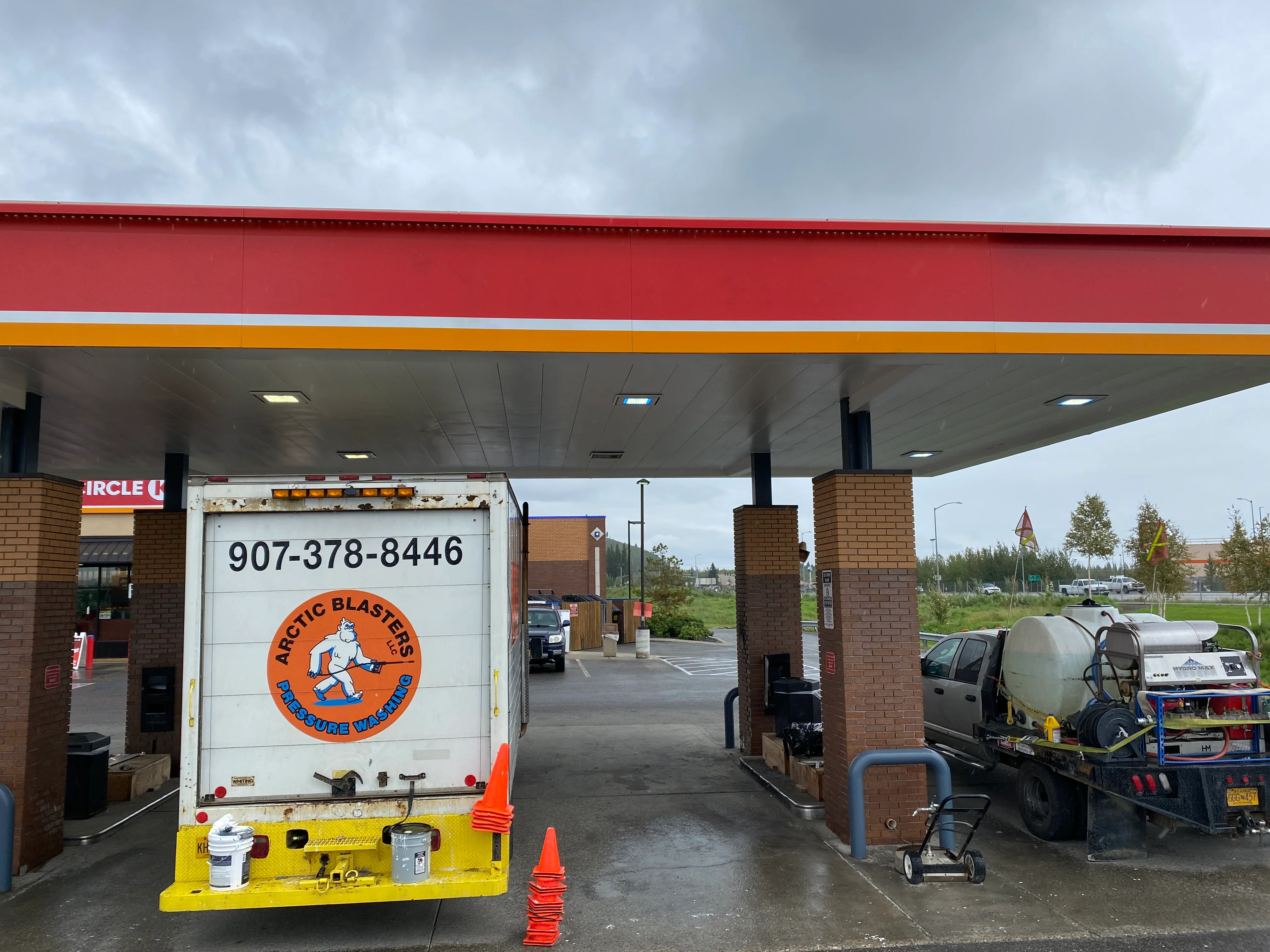 Gas station canopy with red fascia, yellow stripe, brick columns, and concrete pad after pressure washing
